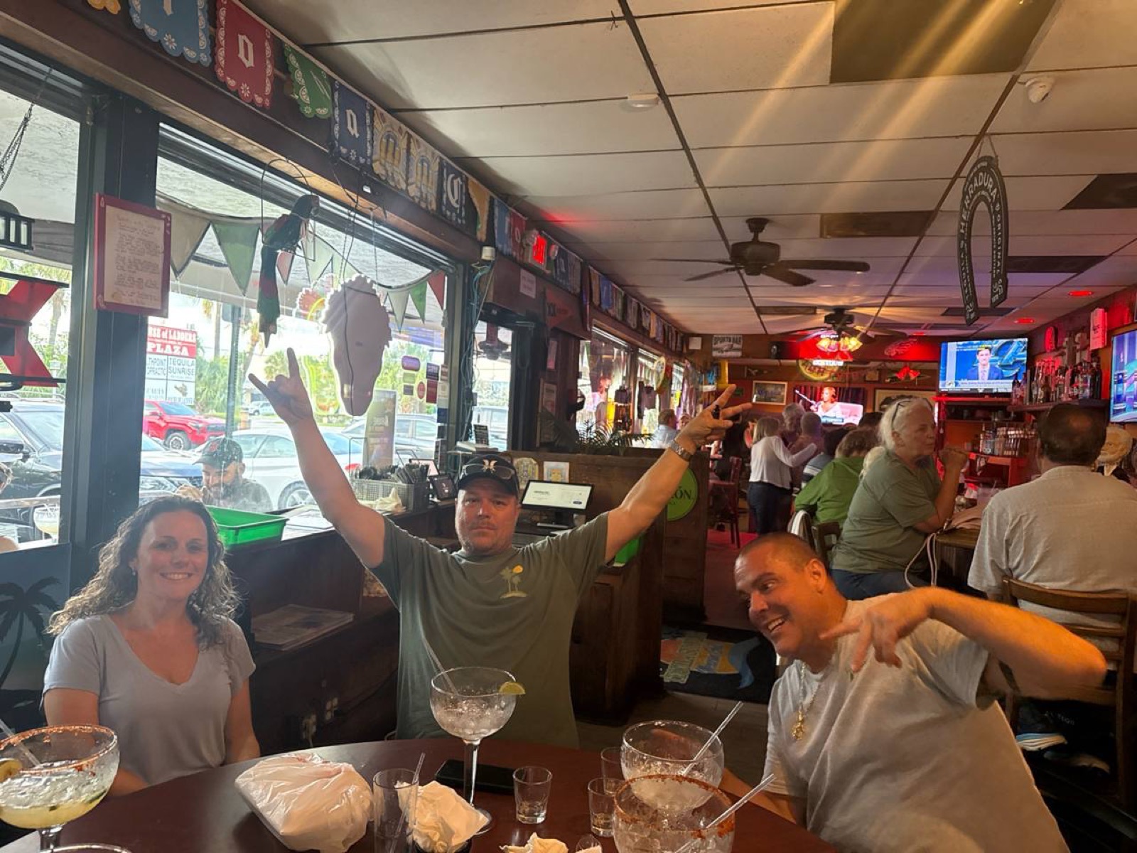 Friends at a lively neighborhood bar table on a Thursday, smiling with margarita glasses.
